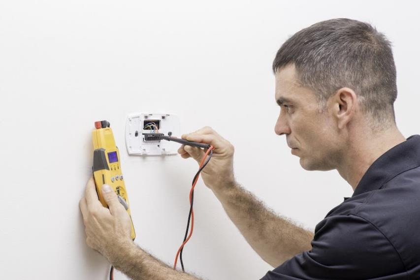 HVAC technician testing thermostat wiring with a multimeter in a Chantilly home